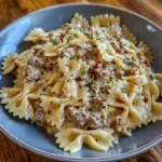A bowl of creamy pasta with ground beef, Parmesan, and fresh herbs on top.